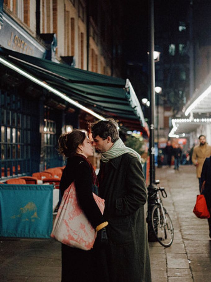 A couple standing forehead to forehead outside a cafe at night