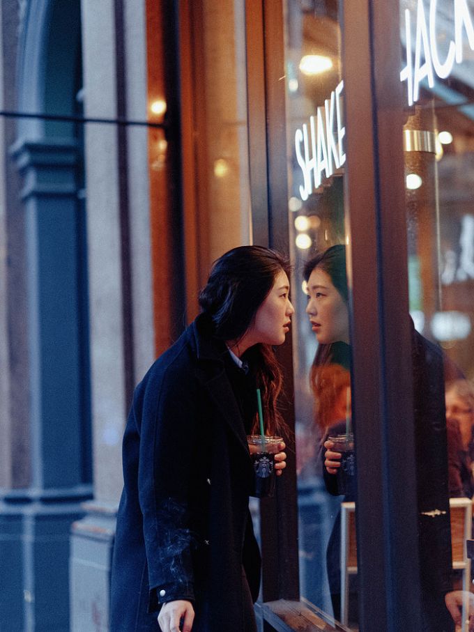 A woman with a drink reflected in a lit shop window