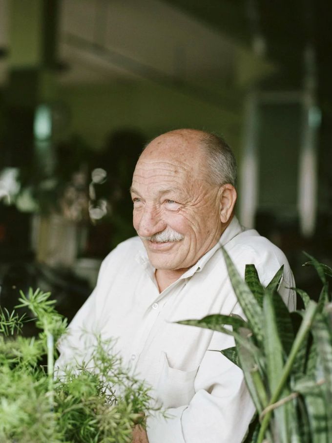 An older man in a white shirt laughing among houseplants